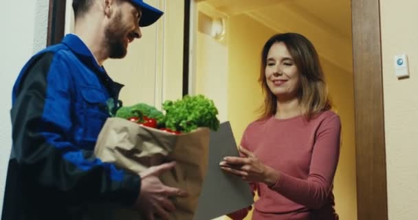 Běloška hezká žena u dveří dostat dodávku čerstvé zeleniny ze supermarketu od mužského kurýra. — Stock video