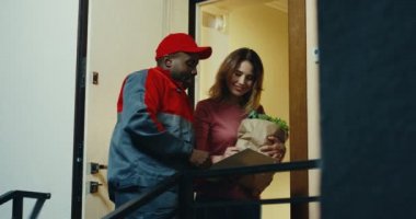 Beyaz bir kadın kuryeden taze sebzeleri alıyor ve imzasını atıyor. İçeride..