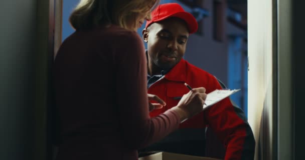 Tył kaukaskiej kobiety podpisującej i odbierającej skrzynkę pocztową od afro-amerykańskiego kuriera firmy przewozowej. — Wideo stockowe