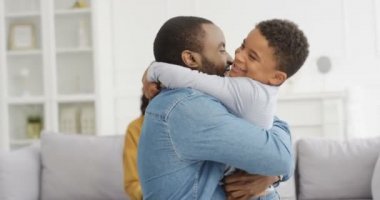 Mutlu Afro-Amerikalı erkek ve kadın küçük sevimli oğullarına sarılıyor ve evinde kanepede gülüyor. Küçük çocuklu neşeli ebeveynler oturma odasında. Anne ve baba gülümsüyor ve çocuğu kucaklıyor..