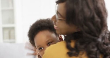 Küçük tatlı Afrikalı Amerikalı kız annesine koşuyor ve oturma odasında kanepede sıkıca sarılıyor. Evin içinde güzel bir çocuğu kucaklayan bir kadının arkası. Annelik aşkı.