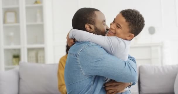 Mutlu Afro-Amerikalı erkek ve kadın küçük sevimli oğullarına sarılıyor ve evinde kanepede gülüyor. Küçük çocuklu neşeli ebeveynler oturma odasında. Anne ve baba gülümsüyor ve çocuğu kucaklıyor.. — Stok video