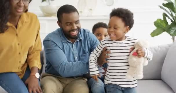 Portrait of young happy African American parents children sitting on sofa smiling cheerfully to camera. Joyful kids with mother and father laughing and having fun on couch in living room. — Stock Video