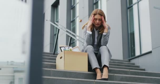 Kaukasiska kvinnliga kontorsarbetare som sitter på trappor i depression med en låda grejer. Arbetslösa affärskvinna förlorade sin verksamhet. Ett ångestfyllt koncept. Arbetslös kvinna i förtvivlan. — Stockvideo
