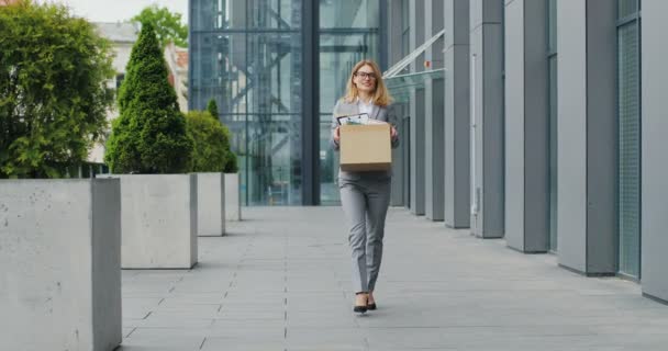 Biała, szczęśliwa bizneswoman chodząca ulicą z pudełkiem rzeczy jak opuszczenie centrum biznesowego i taniec. Pracownica biurowa odeszła z pracy i świętowała. Zwolniona radosna kobieta.. — Wideo stockowe