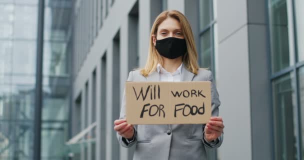 Портрет белой молодой женщины в маске, демонстрирующий плакат со словами, подойдет для еды. Женщина-активистка показывает доску с поиском объявления о работе. Одинокий протест. Безработица в изоляции. — стоковое видео