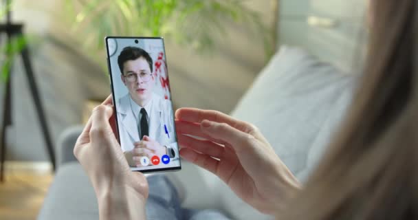 Ragazza che parla con il medico in video chat sul cellulare mentre riposa in camera. Donna che ha un consulto medico online con il medico caucasico in videoconferenza sullo smartphone a casa. Concetto sanitario — Video Stock