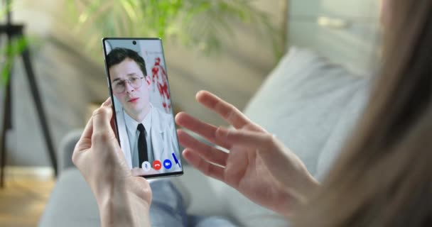 Dívka s lékařskou on-line konzultaci s bělochem lékaře na videokonferenci na smartphone doma. Lékař ukazuje ženské medicíně pacienta ve videohovoru na mobilu. Koncept zdravotní péče — Stock video