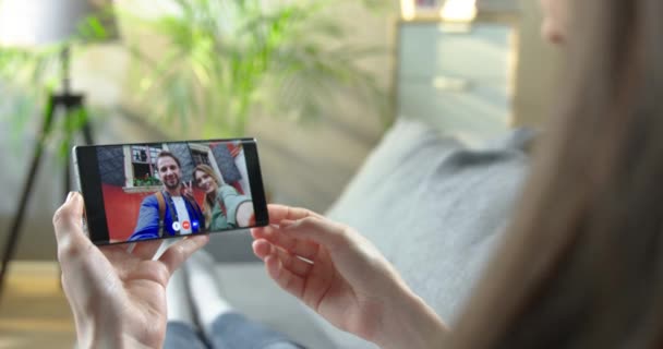 Chica hablando en videoconferencia en smartphone en la sala de estar. Mujer teniendo video conversación con alegres amigos caucásicos hombres y mujeres que están caminando al aire libre en el teléfono celular. concepto de chat en línea — Vídeos de Stock