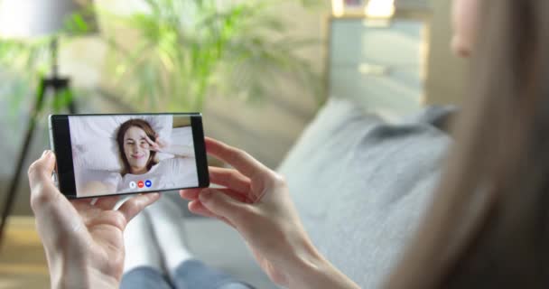 Mujer videochat con un amigo en el teléfono inteligente mientras está sentado en el interior. Mujer teniendo videoconferencia con chica feliz en casa en la cama. Chat de grupo en línea en cuarentena. Concepto de comunicación — Vídeos de Stock