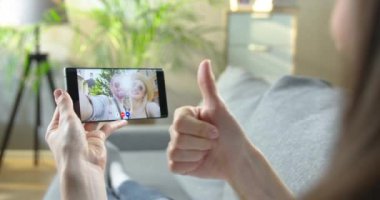 Kadın akıllı telefonda mutlu beyaz bir çiftle video sohbeti yapıyor ve baş parmağını bırakıyor. Kız şehrin dışında duran neşeli erkek ve kadın arkadaşlarıyla görüntülü görüşme yapıyor..