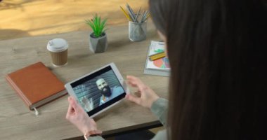 Beyaz erkek arkadaşıyla ofiste otururken görüntülü konuşma yapan bir kadının omzunun üstünden. İş kadını internette el sallayan sakallı adamla webcam üzerinden konuşuyor.