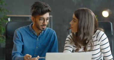 Mulietnik genç adam ve kız ofiste dizüstü bilgisayarın başında birlikte oturuyor ve yeni bir başlangıç projesi üzerinde çalışıyorlar. Karışık ırk erkek ve kadın şirket çalışanları beyin fırtınası yapıyor ve konuşuyor..