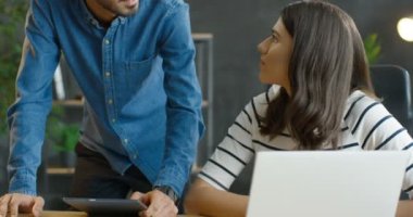 Genç melez erkek ve bayan meslektaşlar ofiste çalışma projesini konuşuyor ve tartışıyorlar. Kafkasyalı bir kız dizüstü bilgisayarla masada oturuyor ve Arap bir adam elinde tablet cihazıyla...