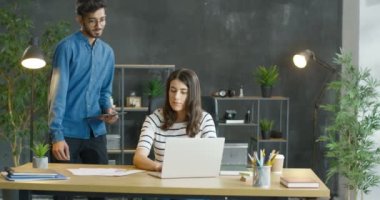 Beyaz bir genç kız ofiste oturuyor ve dizüstü bilgisayarında çalışıyor. Arap adam bayan meslektaşına geliyor ve tablet cihazında bir şey gösteriyor. Ajandada not alan bir kadın. Karışık ırk iş arkadaşları..