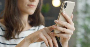 Kredi kartı tutan ve akıllı telefondan alışveriş yapan genç bir bayanı kapatın. Güzel beyaz kız internetten alıyor ve para ödüyor. Kapalı alanda. Cep telefonu ödemesi.