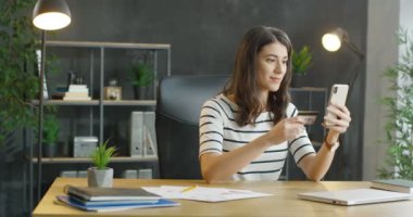 Masasında oturan, kredi kartı tutan ve cep telefonuyla alışveriş yapan beyaz, genç bir ofis çalışanı. Güzel kız internetten alıyor ve tavan arasında ödüyor..