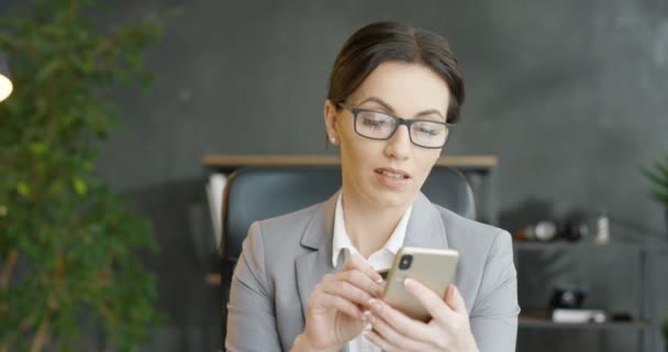 Pengusaha wanita cantik memegang kartu kredit dan belanja online di smartphone saat duduk di kantor. Wanita kaukasia berkacamata membeli di internet dan membayar. Di dalam ruangan. Pembayaran mobile. — Stok Video