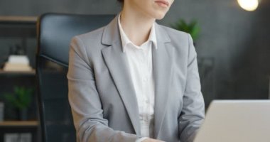 Masada oturup dizüstü bilgisayarla çalışan genç ve güzel bir ofis çalışanı. Çekici esmer, beyaz tenli, gözlüklü iş kadını dolapta klavyede daktilo kullanıyor..