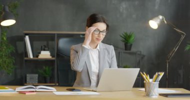 Genç, masada oturmuş dizüstü bilgisayar ve beste yapan, gözlüklü, meşgul, beyaz kadın ofis çalışanı gülümsedi. Çekici iş kadını klavyede yazı yazıyor, mesaj yazıyor, dolapta düşünüyor..