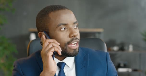 Afrikansk amerikansk seriös affärsman talar på smartphone. Snygg man som talar i mobiltelefon på kontoret. Man som pratar i mobilen. Jobbar i skåpet. Telefonsamtal. — Stockvideo