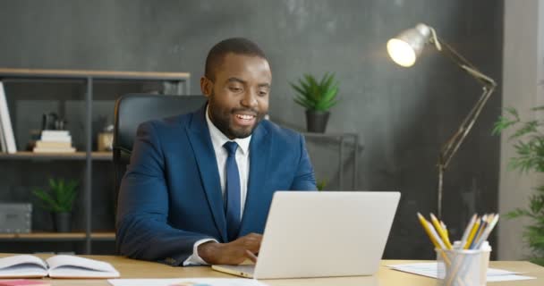 African American busy male office worker sitting at table and having videochat on laptop computer. Attractive businessman talking via webcam. Man in suit and tie working in cabinet. Video call concept — Stock Video