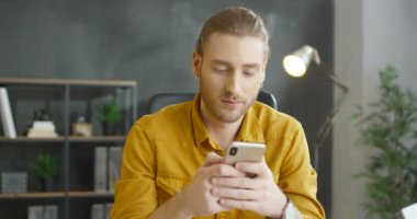 Akıllı telefonu elinde tutan ve düşünen Kafkasyalı genç adama yaklaş. Çatı katındaki cep telefonunu dinleyip kaydıran yakışıklı gülen adam. Cep telefonunda erkek mesajı ve gülümseme..
