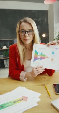 Beyaz tenli, gözlüklü, güzel, sarışın bir kadın. Kameraya grafikler ve çizelgeler gösteriyor. İnternetteki video dersinde açıklayan güzel bayan iş koçu. Hikayeler için dikey yönelim.