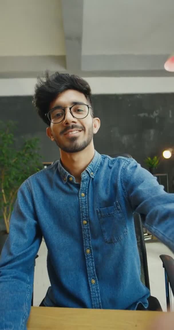 Rekaman orientasi vertikal untuk cerita. Pemuda Arab tampan dengan kemeja jins biru duduk di meja dan tersenyum ke kamera. Pria Arab memberikan jempol dan berpose. — Stok Video