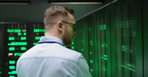 Zadní běloch v brýlích, procházející se mezi servery s notebookem a kontrolující práci velkých datových procesorů. Zadní pohled. Mužská analytika v ukládání dat při práci na zabezpečení informací. — Stock video