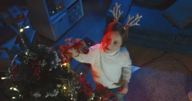 Kış tatilinden önce, sıcacık karanlık odada Noel ağacı süsleyen küçük beyaz kızın yukarıdan görünüşüne bak..