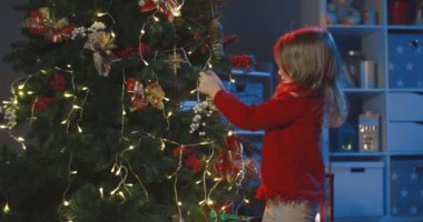 Kırmızı kazaklı beyaz kız tatilden önce evde Noel ağacı süslüyor..