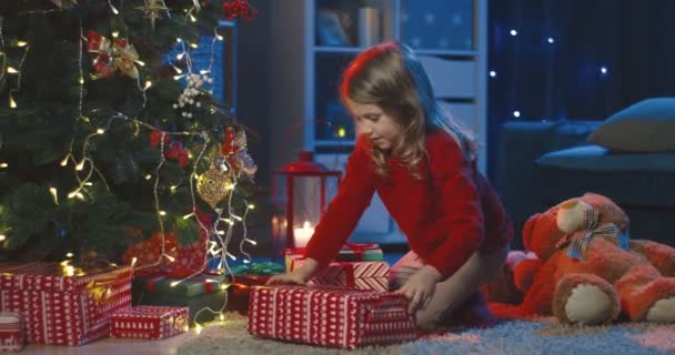 身着红色毛衣的有趣而漂亮的白人女孩在圣诞树下享受礼物时的画像. — 图库视频影像