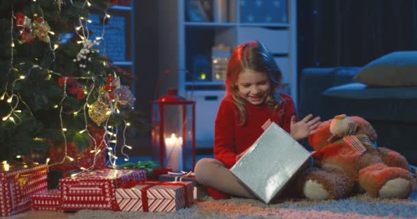 圣诞前夕，快乐可爱的小女孩一边打开礼物，一边在装饰过的树上玩乐。在家里. — 图库视频影像