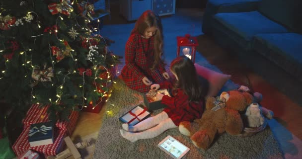 Vista dall'alto sulle due piccole ragazze caucasiche sedute sul pavimento la vigilia di Natale all'albero e che tirano fuori i giocattoli dell'albero di x-mas dalla scatola. — Video Stock