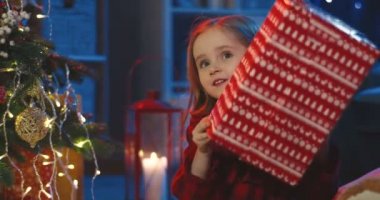 Kafkasyalı küçük şirin kızın büyük Noel hediyesini paketleyip mutlu olduğu yakın plan. Evde, Noel ağacında..