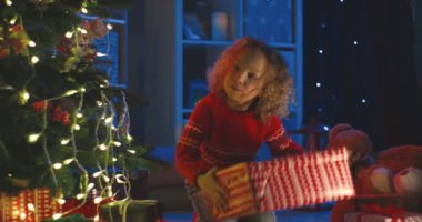 Güzel kıvırcık kızın Noel hediyesiyle birlikte Noel ağacını açarken çekilmiş bir portre resmi..