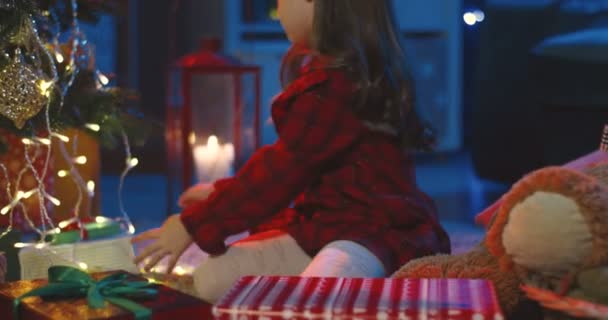 Bella piccola ragazza caucasica con i capelli lunghi seduti nella stanza accogliente buio sul pavimento e decorato x-mas albero con ghirlande. — Video Stock