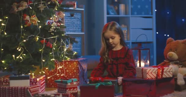 Portrait de la petite écolière caucasienne prenant un jouet de la boîte et décorant arbre de Noël avec elle dans la chambre confortable avant la veille de Noël. — Video