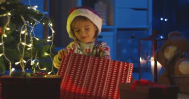 Noel Baba şapkalı şirin beyaz çocuğun portresi. Noel hediyesi oyuncak ayısıyla mutlu oluyor. Geceleri ağaçta sarılıyor..