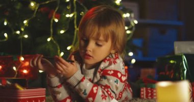 Noel ağacında elinde bir kalemle Noel hediyelerinin arasında uzanan tatlı beyaz çocuk..