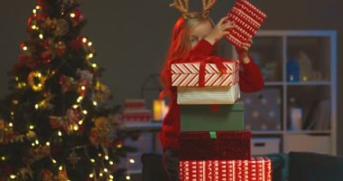 Küçük sarışın komik kız Noel ağacının rahat odasında birbirinin üstüne bir sürü Noel hediyesi koyuyor..