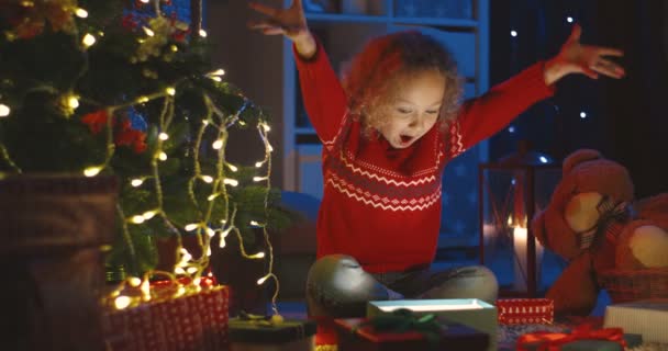 Прекрасный счастливый кавказский кудрявый малыш открывает коробку с подарком на Рождество от Санты и достает смартфон на рождественской елке ночью. — стоковое видео