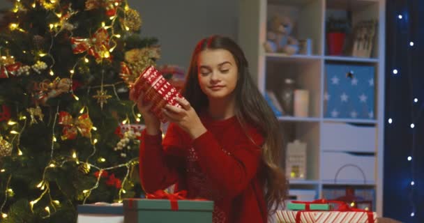 Ritratto della ragazza adolescente caucasica seduta a tavola e che guarda i regali x-mas all'albero di Natale. — Video Stock