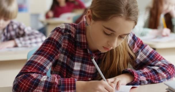 Gros plan de l "écolière adolescente caucasienne aux cheveux blonds écrivant dans le copybook un exercice et réfléchissant à la leçon à l'examen. — Video