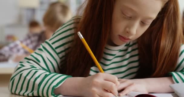 Close-up van de Kaukasische tiener schattig roodharig schoolmeisje schrijven in de copybook een oefening op de les examen in de school. — Stockvideo