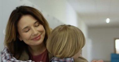 Beyaz görünümlü genç bir anne koridorda onu okula getirirken küçük tatlı oğluna sarılıp hoşça kal diyor. Kapat..