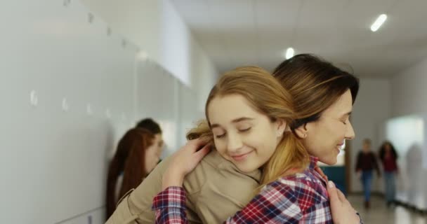 Hübsche kaukasische junge Frau Mutter des charmanten Teenie-Mädchens, das ihre Tochter zur Schule bringt, sich verabschiedet und umarmt, Mädchen kommt ins Klassenzimmer. — Stockvideo