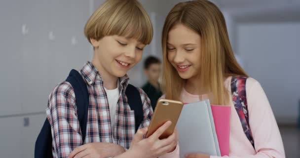 Roztomilý kavkazský dospívající spolužáci, dívka a chlapec, stojící ve škole na přestávce a školák ukazuje něco na dívku na smartphonu. — Stock video