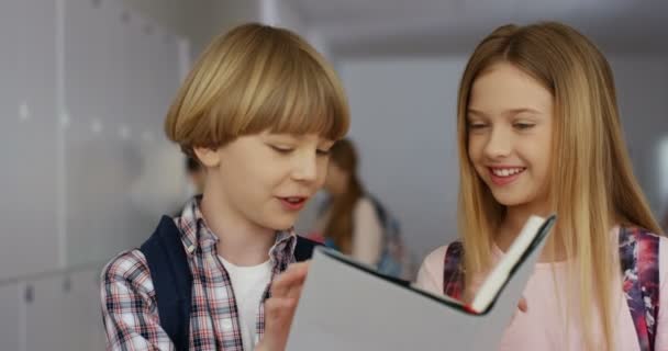 Detailní záběr na roztomilé děti chlapec a dívka, žáci stojící na přestávce ve škole a vesele se dívá do učebnice. — Stock video